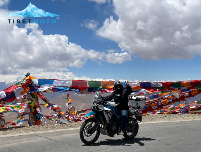 Motorradfahrer fährt vorbei an Gebetsfahnen in Tibet